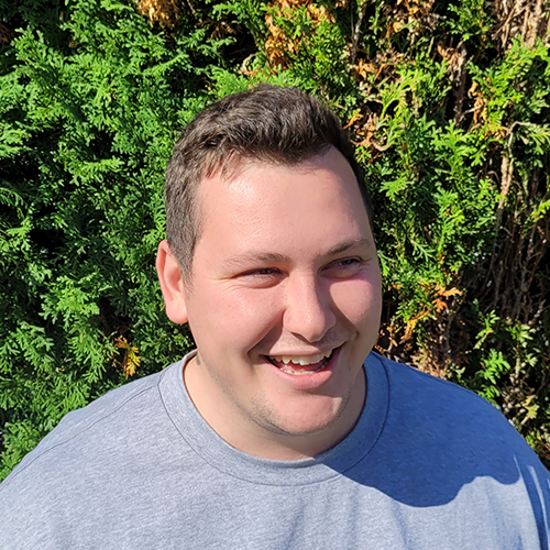 A man wearing a grey tshirt looks off to the side of camera and smiles.